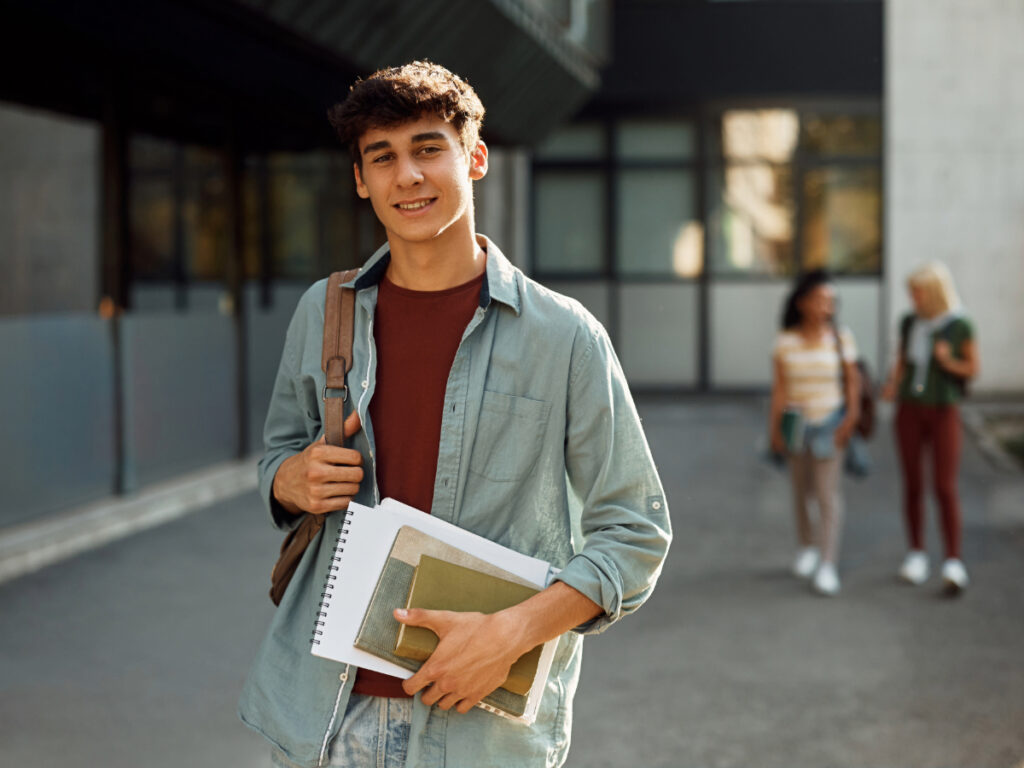 College Student on campus holding books with backpack on and other students walking in background for article Higher Education Opportunities in Portland for newcomers moving to Portland.