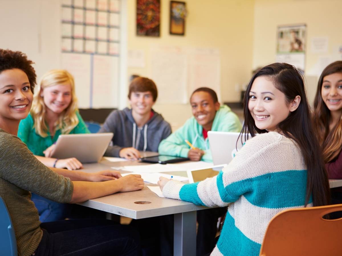 Group of 6 diverse high school students sitting together at a table with papers, laptops and working on a project together for article Catlin Gabel for newcomers moving to Portland.