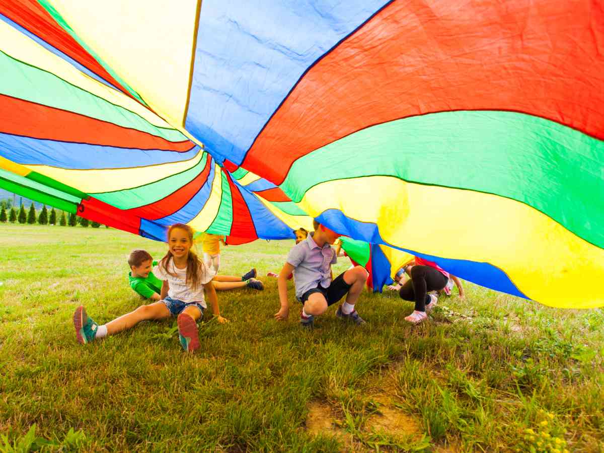 Photo of kids under rainbow colored parachute on grass for article Horizon Christian Schools for newcomers moving to Portland.