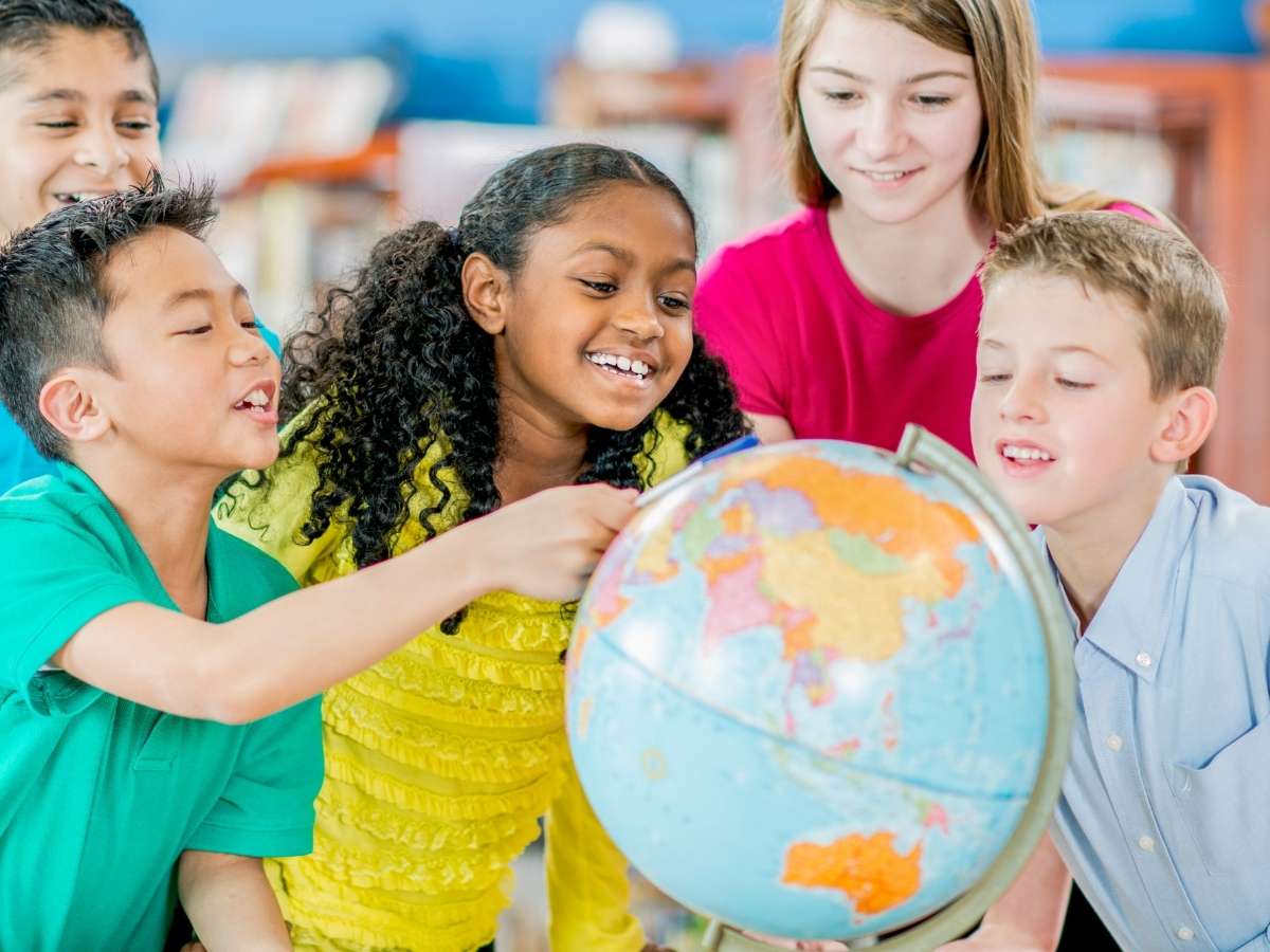 5 kids smiling looking at a world globe for article Gresham-Barlow School District for newcomers moving to Portland area.