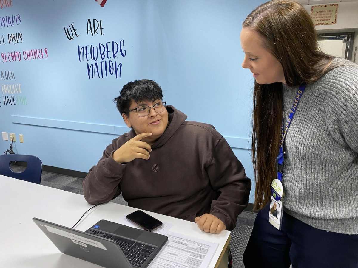 Student working on computer looking up at teacher who is helping for article Newberg School District for newcomers moving to Portland area.