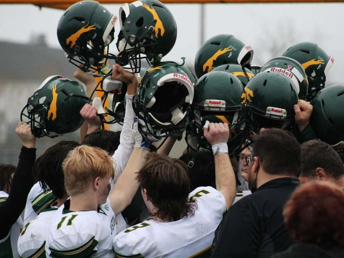 The football team celebrating in a huddle with helmets held high for article Gaston School District for newcomers moving to Portland area.