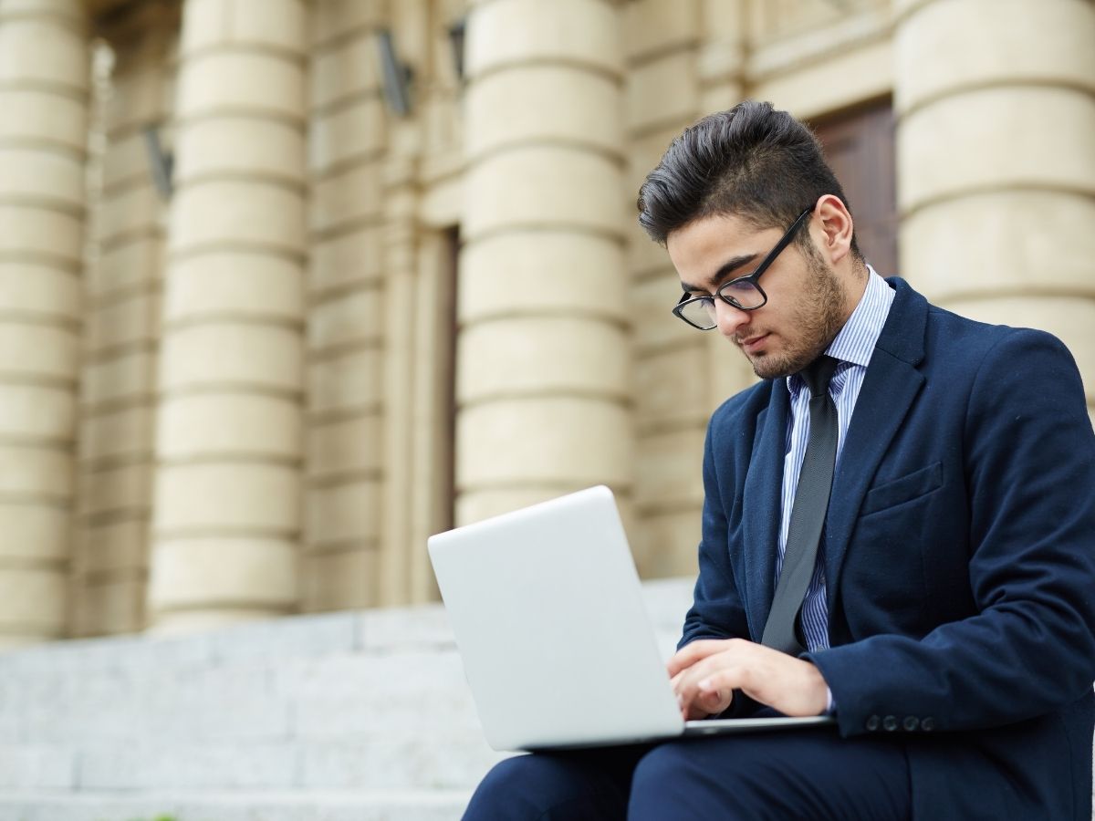 Man in business suite on laptop sitting outdoors on steps of building for article finding the right job in Portland for newcomers moving to Portland.
