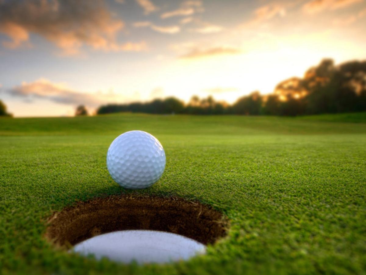 Close up shot of golf ball on edge of going in the hole with sunset in background at King City Golf Club for newcomers moving to Portland.