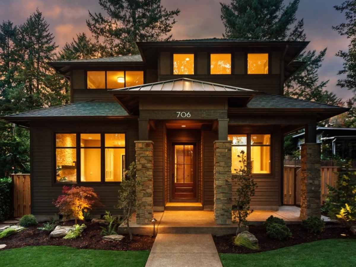 2 Story home with lots of windows and gorgeous curb appeal with all the lights on inside making it glow with trees behind it and green grass in front for article Homes as Beautiful as They Are Efficient for newcomers moving to Portland.