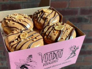 Close up of box of 4 Makin ' Me Bananas Donuts - Banana fluff filling with peanut butter, chocolate, peanuts + banana chip on top at VooDoo Doughnut for article Food Carts, Donuts, and Ice Cream in Portland for newcomers moving to Portland.