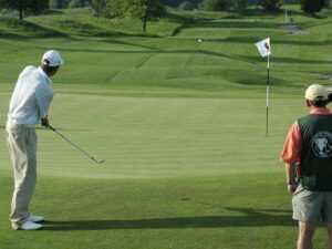 Man chipping a golf ball onto the green with caddy watching for article Golf courses in the Portland area for newcomers moving to Portland.