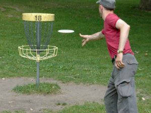 Man throwing disc at disc golf basket labeled #18 for article Disc Golf in Portland for newcomers moving to Portland.