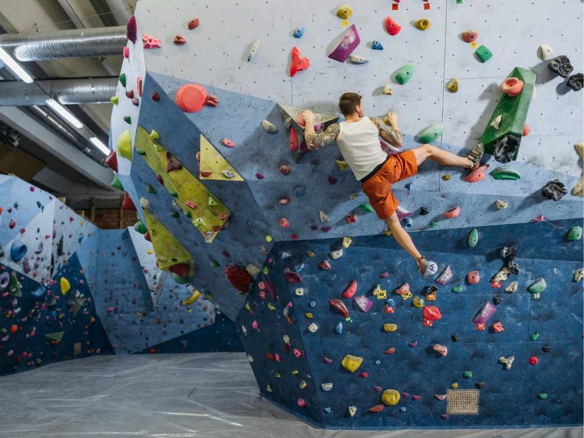 Stock photo image of man in white tank top and orange shorts bouldering at an indoor rock climbing facility for article Portland Rock Climbing for newcomer moving to Portland.