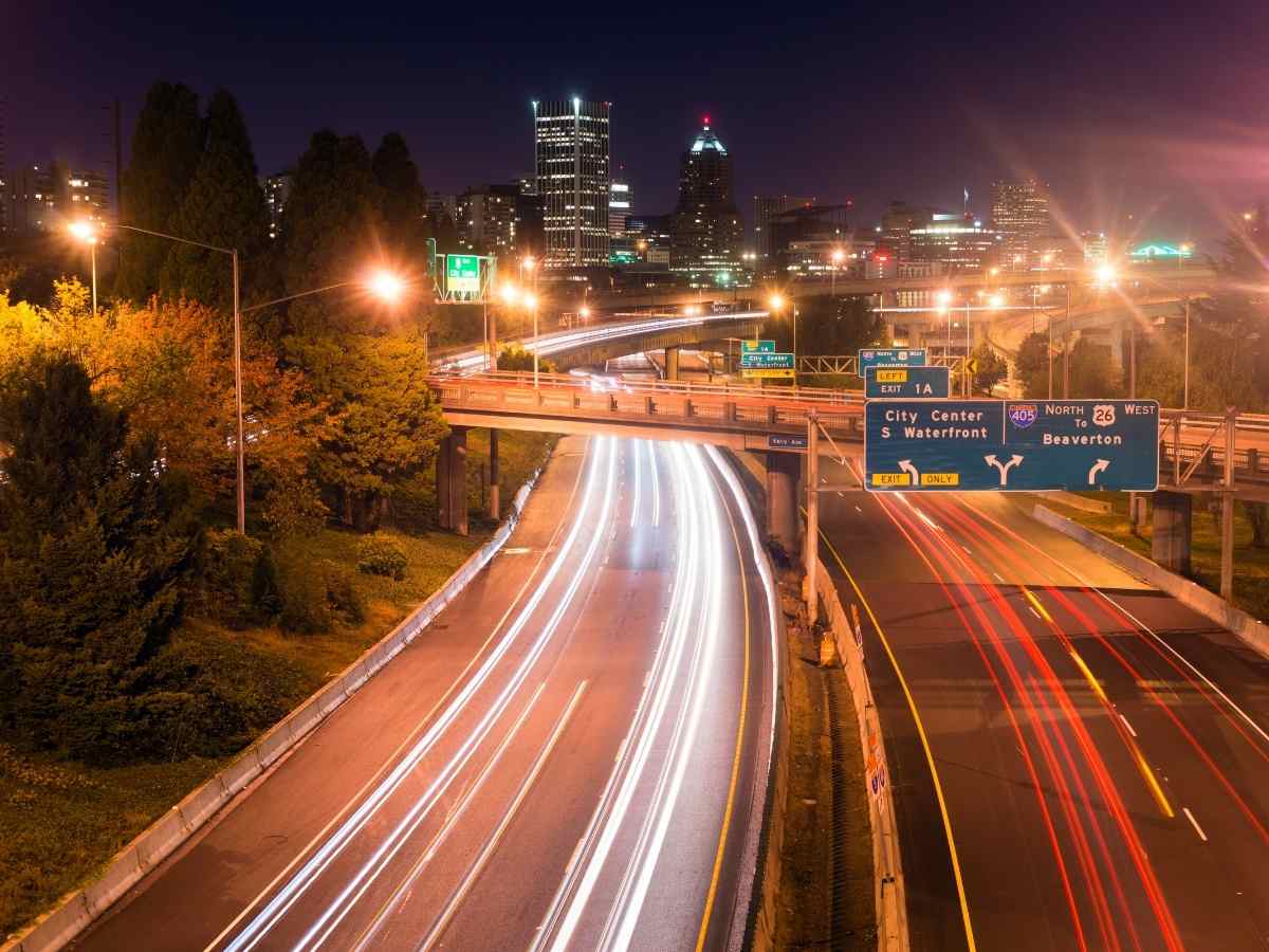 Portland interstates at night with light streaks on the road from time-lapse of cars headlights and city in the background for article How to Get Around Portland for newcomers moving to Portland.