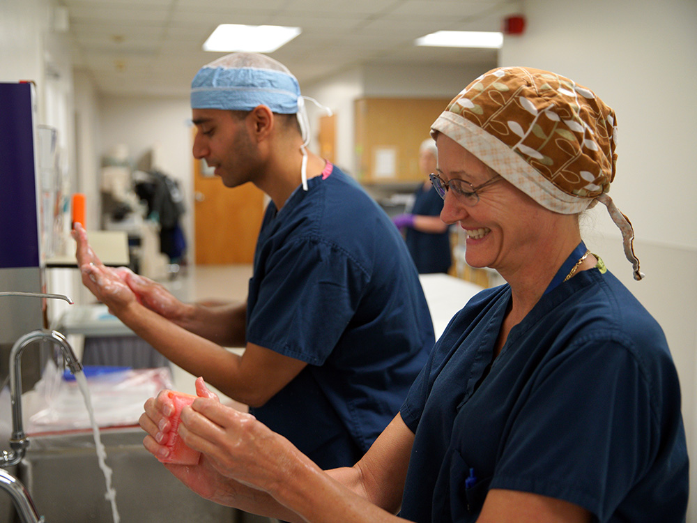Male and female doctors in navy scrubs washing and scrubbing hands prior to surgery for article The Portland Clinic for newcomers moving to Portland.