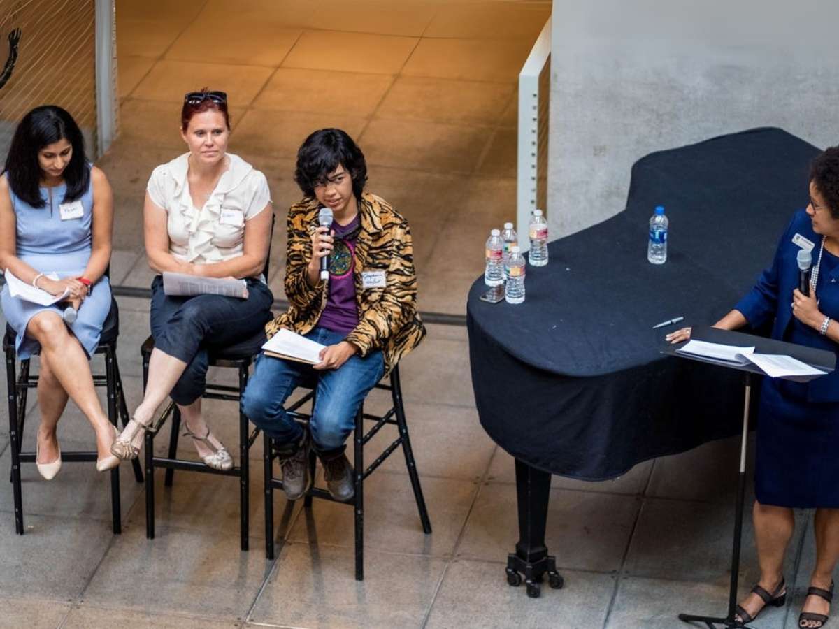 PDXWIT Women on a panel sitting on stools - one with a microphone speaking with a moderator standing on the right side next to a grand piano with a podium with notes on it for article Technology Association of Oregon for newcomers moving to Portland.
