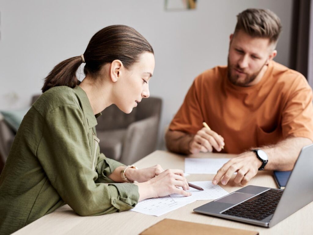 Girl sitting at a table with papers and laptop while tutor sits next to her pointing at the papers in front of the student for article Find the Right Tutor in Portland for newcomers moving to Portland.