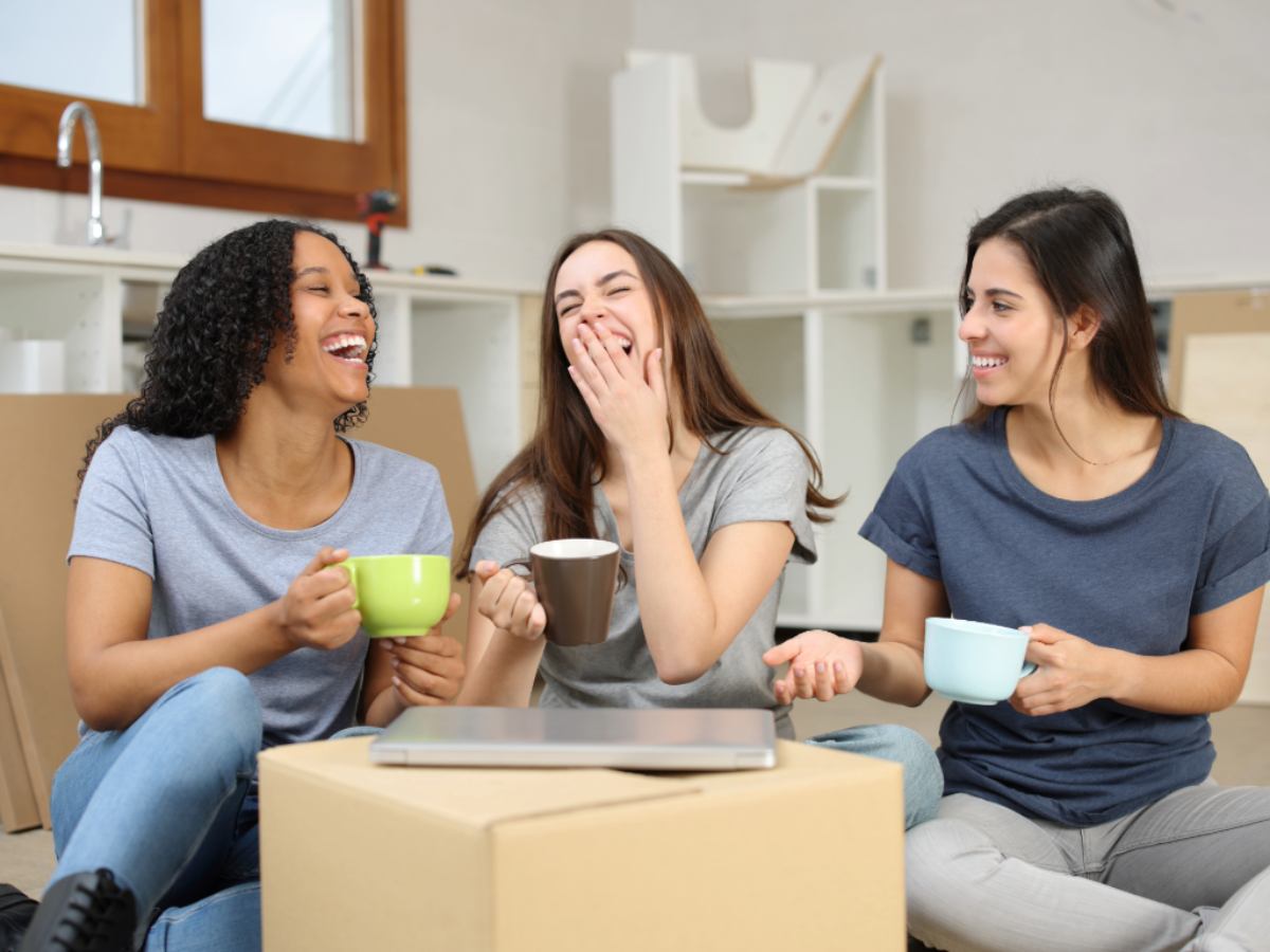 3 female roommates sitting on floor drinking coffee with moving boxes around them for article Finding Roommates in Portland for newcomers moving to Portland.