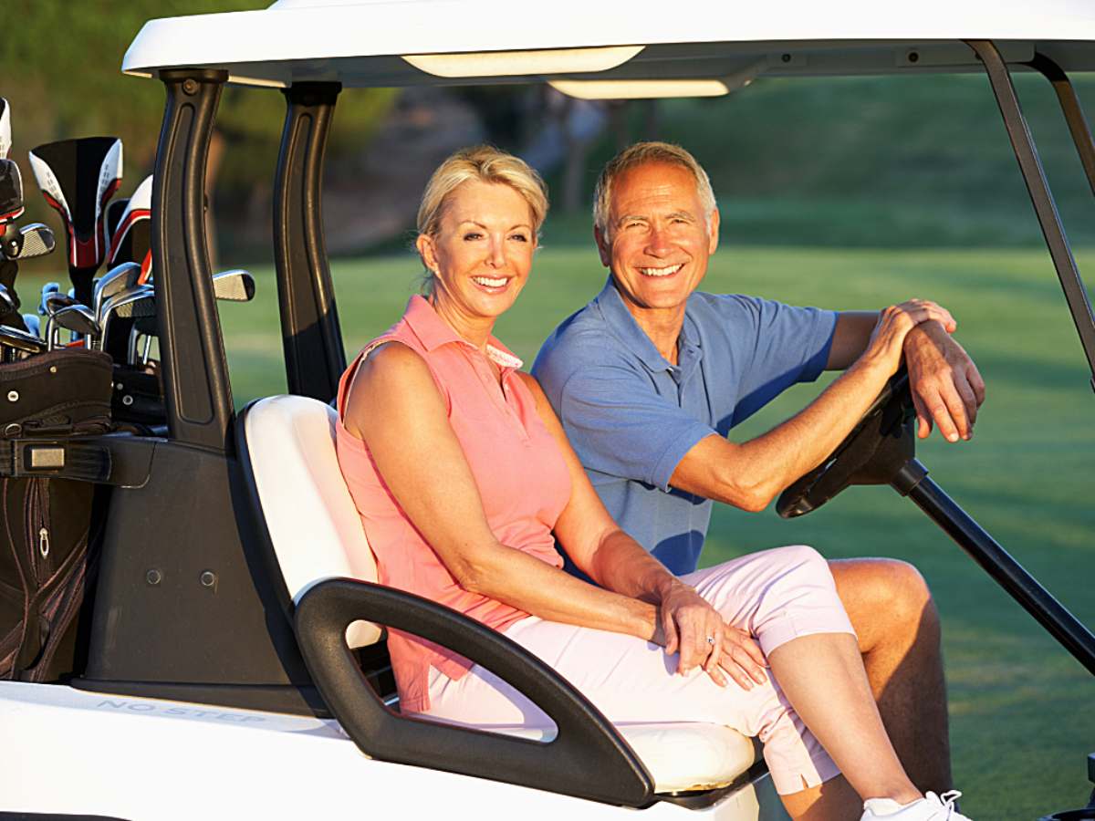 A man and woman in a golf cart on a golf course smiling at the camera for article - Tee Off in Paradise: Portland's Top Golf Courses for Retirees for newcomers retiring in Portland.