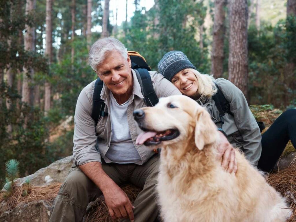 Active senior couple posing with their golden retriever dog while hiking out in the pacific northwest mountains with large pine trees around them for article Pet-Friendly Retirement Living in Portland: 7 Great Places for Newcomers moving to Portland.