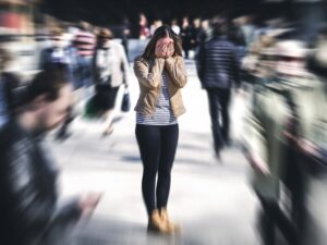 Woman standing in center of walkway with her hands over her face and a blur of people going by her for article Mental Health Services in Portland in 2025 for newcomers moving to Portland.