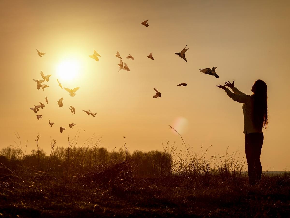 Silhouette of woman releasing birds during sunrise on coast for article Faith & Community: 10 Spiritual Centers in Portland for newcomers moving to Portland.