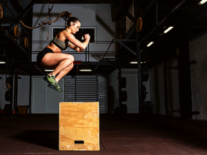 Girl box jumping at CrossFit gym.