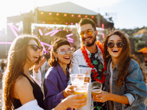 Group of young adults laughing and cheering their beers at an outdoor festival.