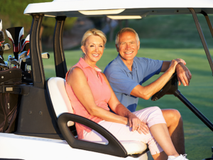 A man and woman in a golf cart on a golf course smiling at the camera.